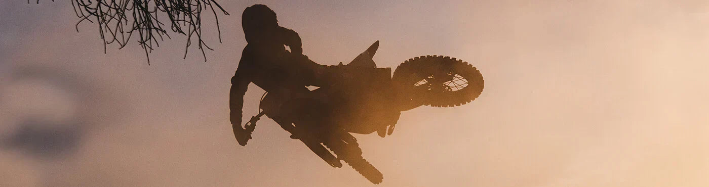 Silhouette einer Person, die vor dem Hintergrund eines Sonnenuntergangs auf einem Motocross-Motorrad einen Stunt in der Luft ausführt.