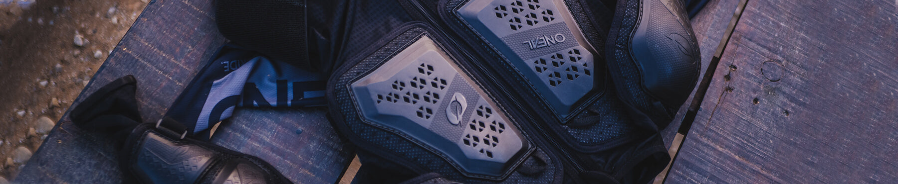 Nahaufnahme einer schwarzen Sportschutzweste mit gepolsterten Bereichen und Belüftungslöchern, die auf einer Holzoberfläche liegt. Auf einem Teil der Weste ist der Markenname „Zeno“ zu sehen.