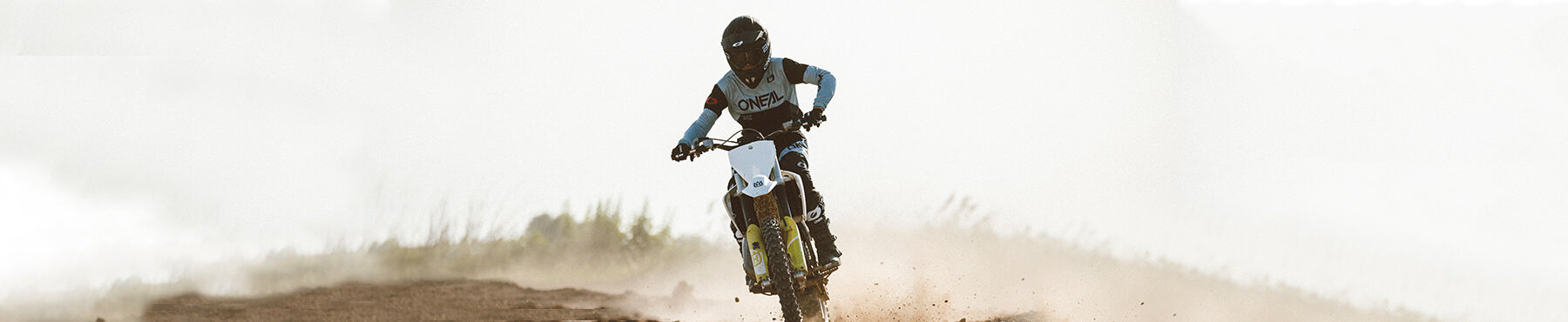 Ein Motorradfahrer in Schutzkleidung fährt mit einem Dirtbike auf einem staubigen Pfad vor dem dunstigen Hintergrund.
