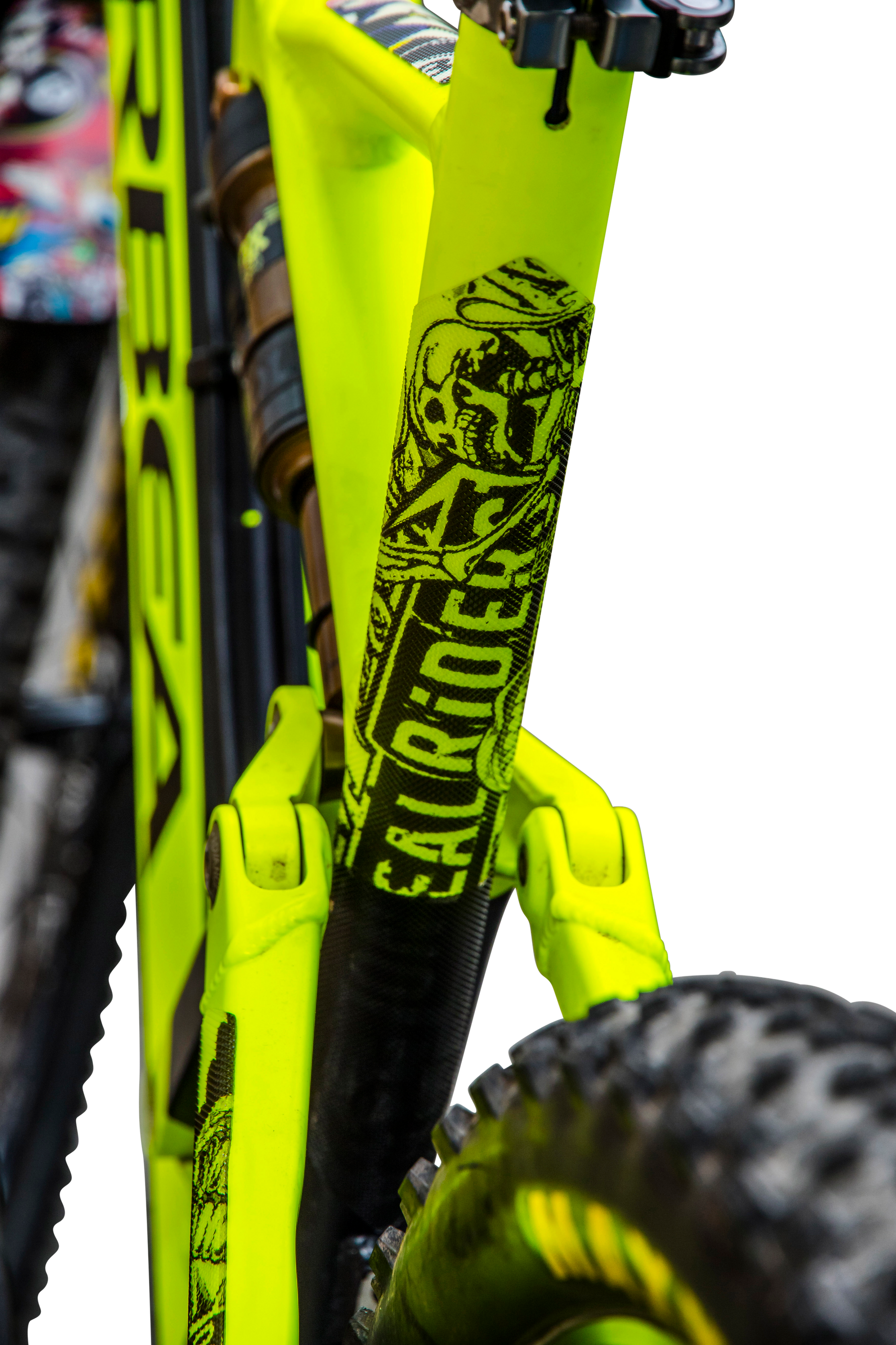 Nahaufnahme eines mit AZONIC FRAME GUARDS ausgestatteten, leuchtend gelben Mountainbike-Rahmens von AZONIC mit auffälligen schwarzen Grafiken und dem Schriftzug "EAT RICE" auf dem Unterrohr; Hinterradreifen und Federung sind ebenfalls zu sehen.