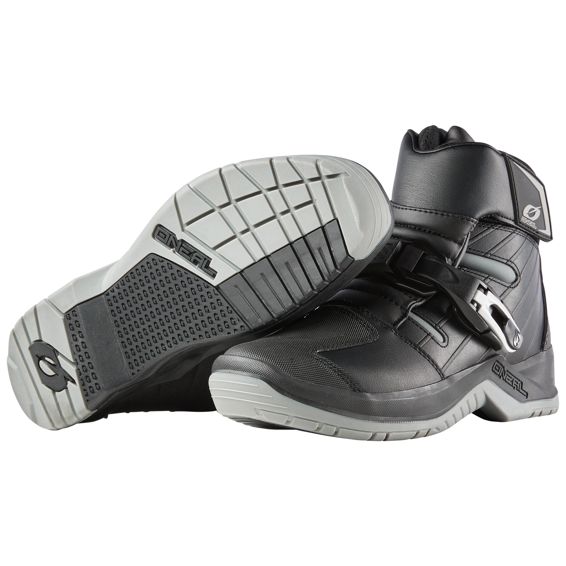 Ein Paar O'NEAL RMX SHORTY Stiefel in Schwarz und Grau - ein Stiefel steht aufrecht, der andere liegt auf der Seite, um die strukturierte Sohle und die Verschlussschnalle zu zeigen - ideal für bequemes Tragen auf dem Motorrad.