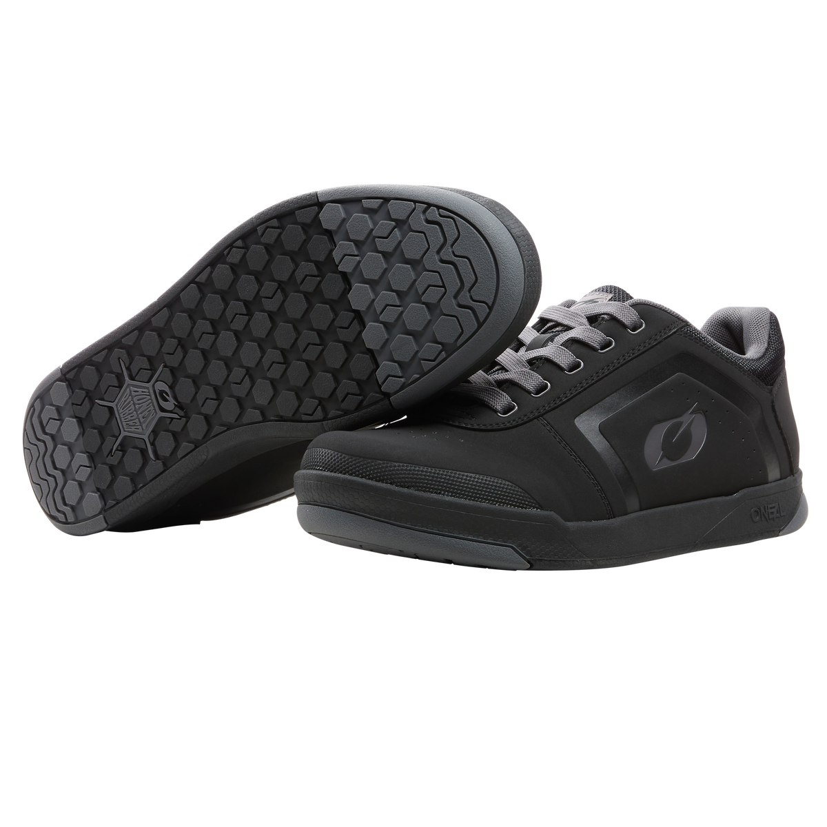 Ein Paar O'NEAL PINNED FLAT Pedal Schuhe in Schwarz mit dunkelgrauer Sohle, die einen sechseckigen Griff für Flat-Pedal-Fahrten aufweisen. Ein Schuh steht aufrecht und zeigt die Seite und Schnürsenkel; der andere kippt, um die strukturierte Sohle zu zeigen.