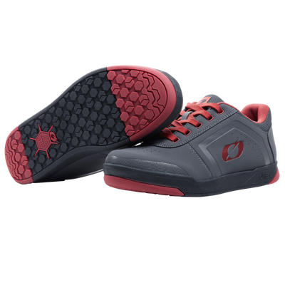 Ein Paar O'NEAL PINNED FLAT Pedal Schuhe in Grau mit roten Sohlen und Schnürsenkeln. Ein Schuh steht aufrecht, während der andere ein schwarzes und rotes Profil aufweist, das bei Fahrten mit flachen Pedalen optimalen Halt bietet. Marke: O'NEAL.