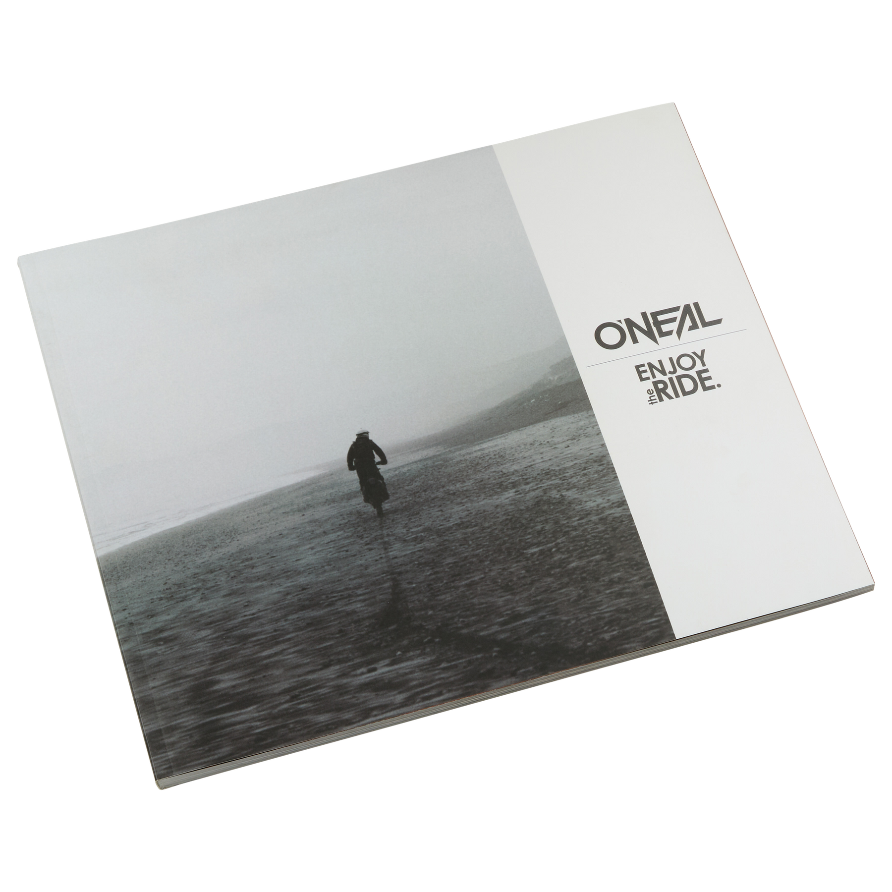 Das geschlossene O'NEAL ENJOY THE RIDE BOOK zeigt eine einsame Figur an einem nebligen Strand, die Emotionen hervorruft. Auf der rechten Seite ist das O'NEAL-Logo und der Schriftzug "ENJOY THE RIDE." in Schwarz auf Weiß zu sehen. Marke: O'NEAL. Produkt: O'NEAL ENJOY THE RIDE BOOK (KOSTENLOSER GOODIE-WAGEN).