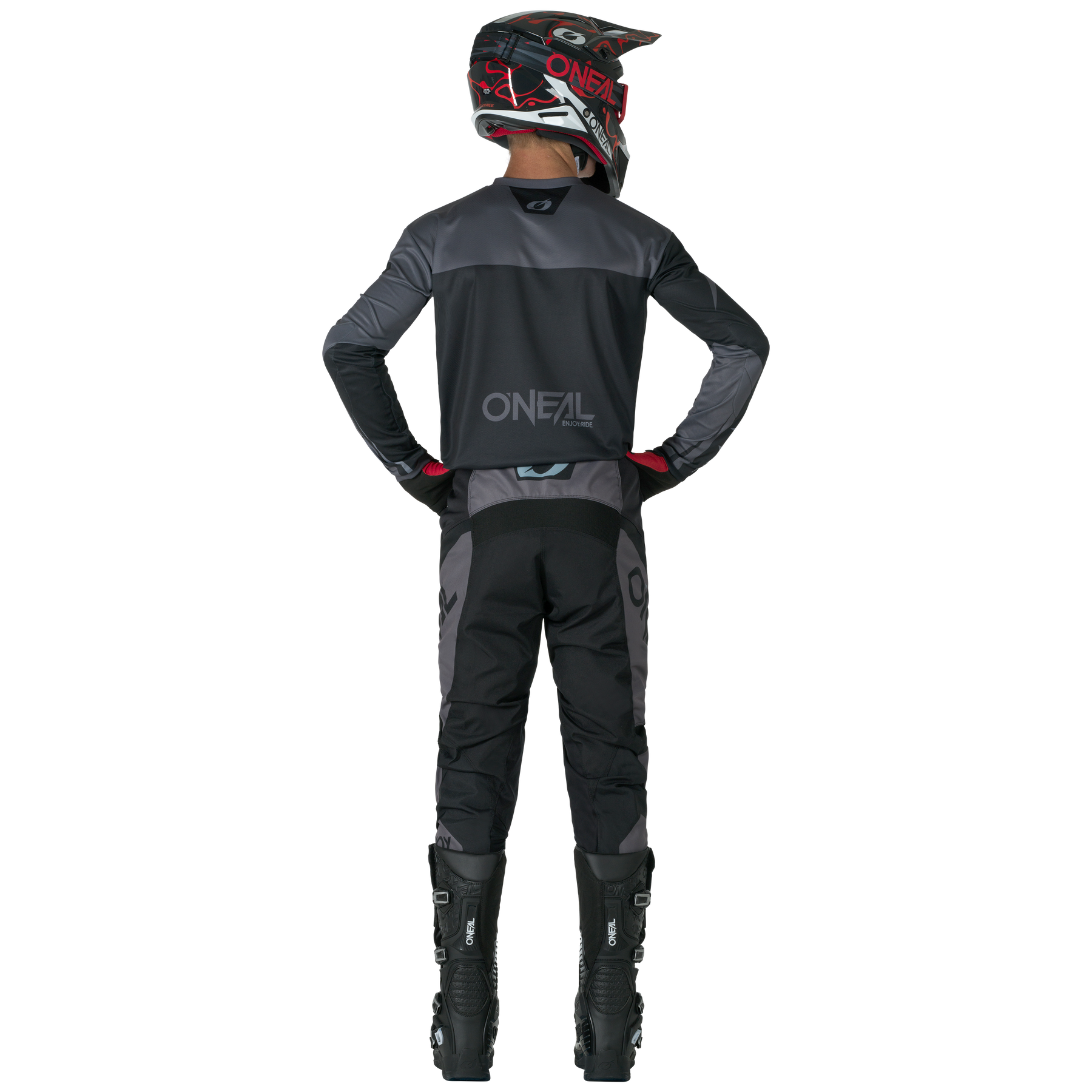 Eine Person in schwarzer und grauer Motocross-Ausrüstung steht mit den Händen in den Hüften, trägt ein O'NEAL-Trikot, hohe schwarze Stiefel und O'NEAL ELEMENT Pants RACEWEAR.