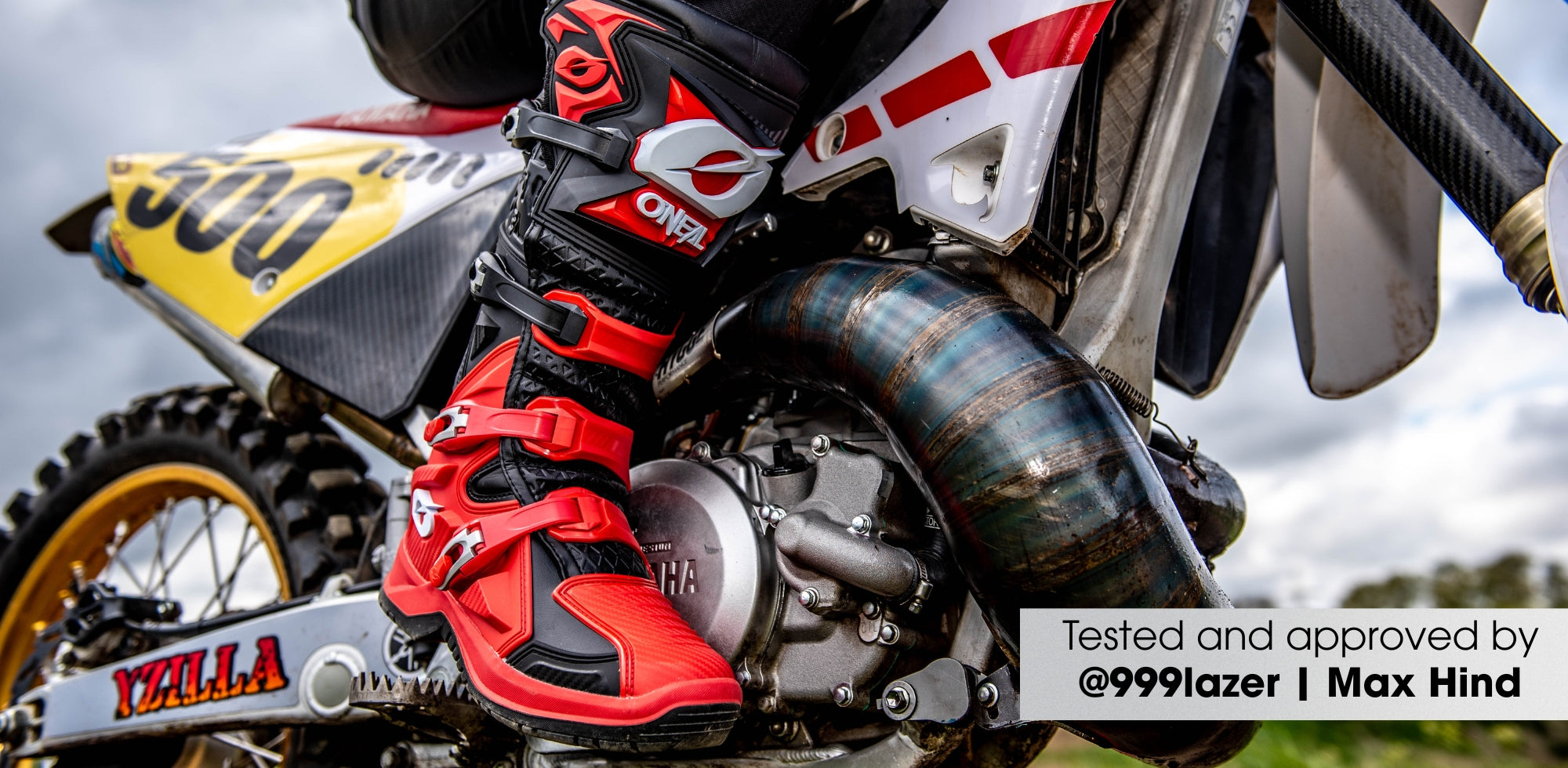 Nahaufnahme einer Person mit roten und schwarzen Motocross-Stiefeln auf einem Yamaha-Dirtbike, die Details des Motorrads und den Auspuff zeigt; Textüberlagerung: "Getestet und genehmigt von @999lazer | Max Hind.