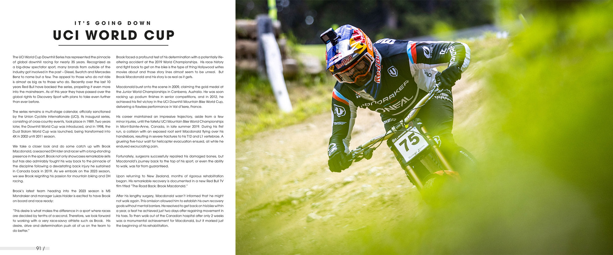 Ein Radfahrer mit Helm, Kamera und Startnummer 75 rast einen Feldweg hinunter. Der Radfahrer trägt Schutzkleidung. Im Hintergrund sind Grünflächen und Teile des Weges zu sehen, im Vordergrund ist ein Unschärfeeffekt zu sehen. Hinweis: Der Text ist unleserlich.