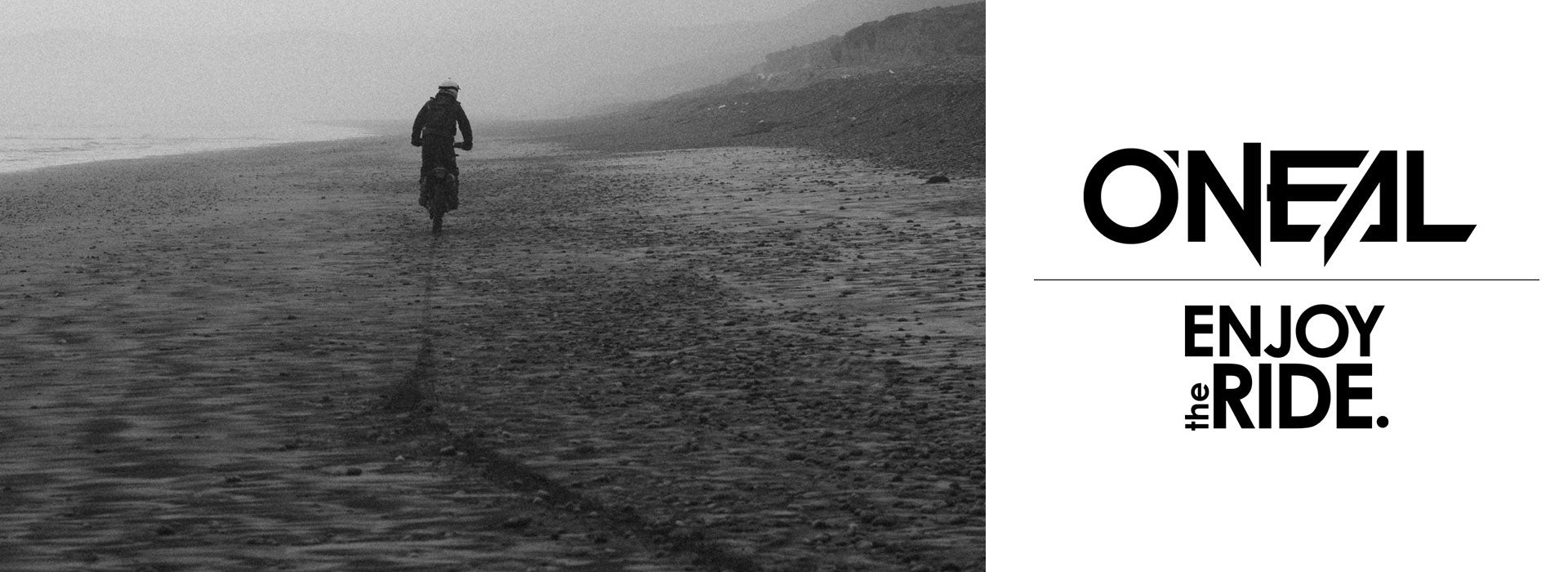 Eine Person fährt mit einem Motorrad an einem verlassenen, nebligen Strand entlang und hinterlässt eine Spur im Sand. Das Bild ist schwarzweiß. Auf der rechten Seite steht „O’NEAL“, gefolgt von „ENJOY the RIDE.“ in fetter Typografie.