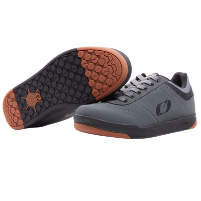 Ein Paar graue O'NEAL PUMPS FLAT Schuhe mit schwarzen Schnürsenkeln und Sohlen mit sechseckigem Profil, braunen Akzenten an der Ferse und der Spitze, einem Logo an der Seite und einem auf der Seite ausgestellten Schuh als Detail. Marke: O'NEAL.