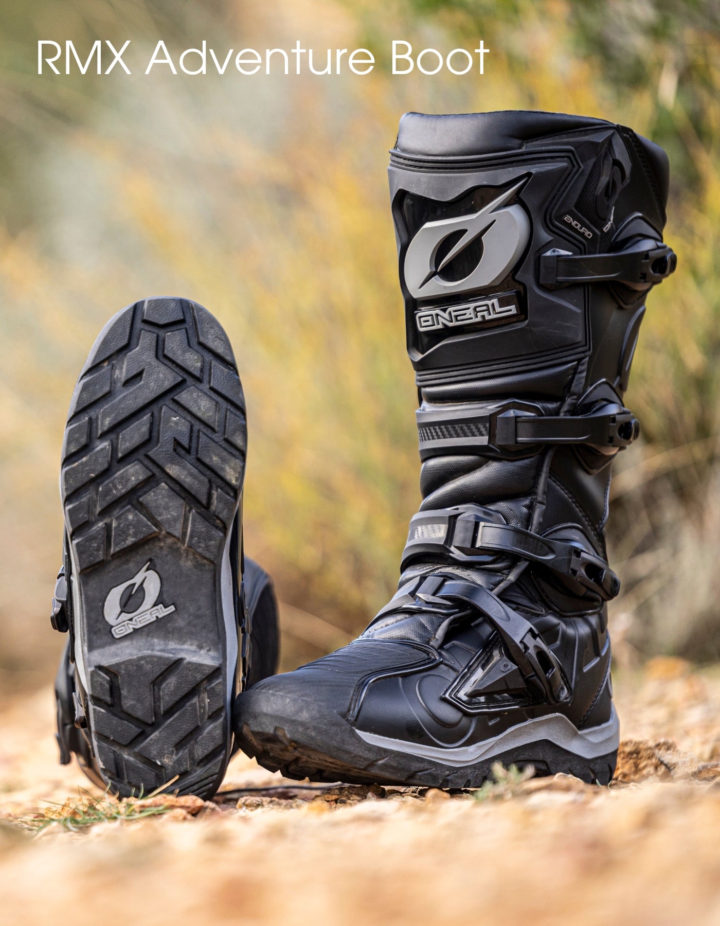 Abgebildet ist ein Paar schwarze O'Neal RMX Adventure Boots; ein Stiefel steht aufrecht, während der andere geneigt ist, um die robuste Sohle zu zeigen. Der Hintergrund ist im Freien und unscharf, mit der Aufschrift "RMX Adventure Boot" am oberen Rand.