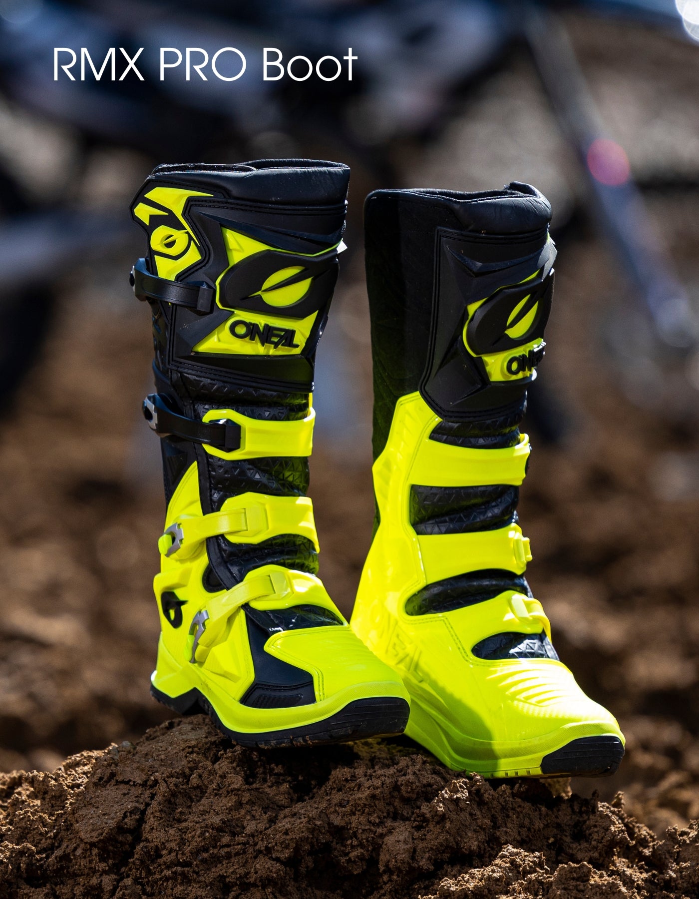Ein Paar leuchtend gelber und schwarzer Motocross-Stiefel mit der Aufschrift "ONEAL" stehen aufrecht im Dreck, mit dem Text "RMX PRO Boot" in der oberen linken Ecke.