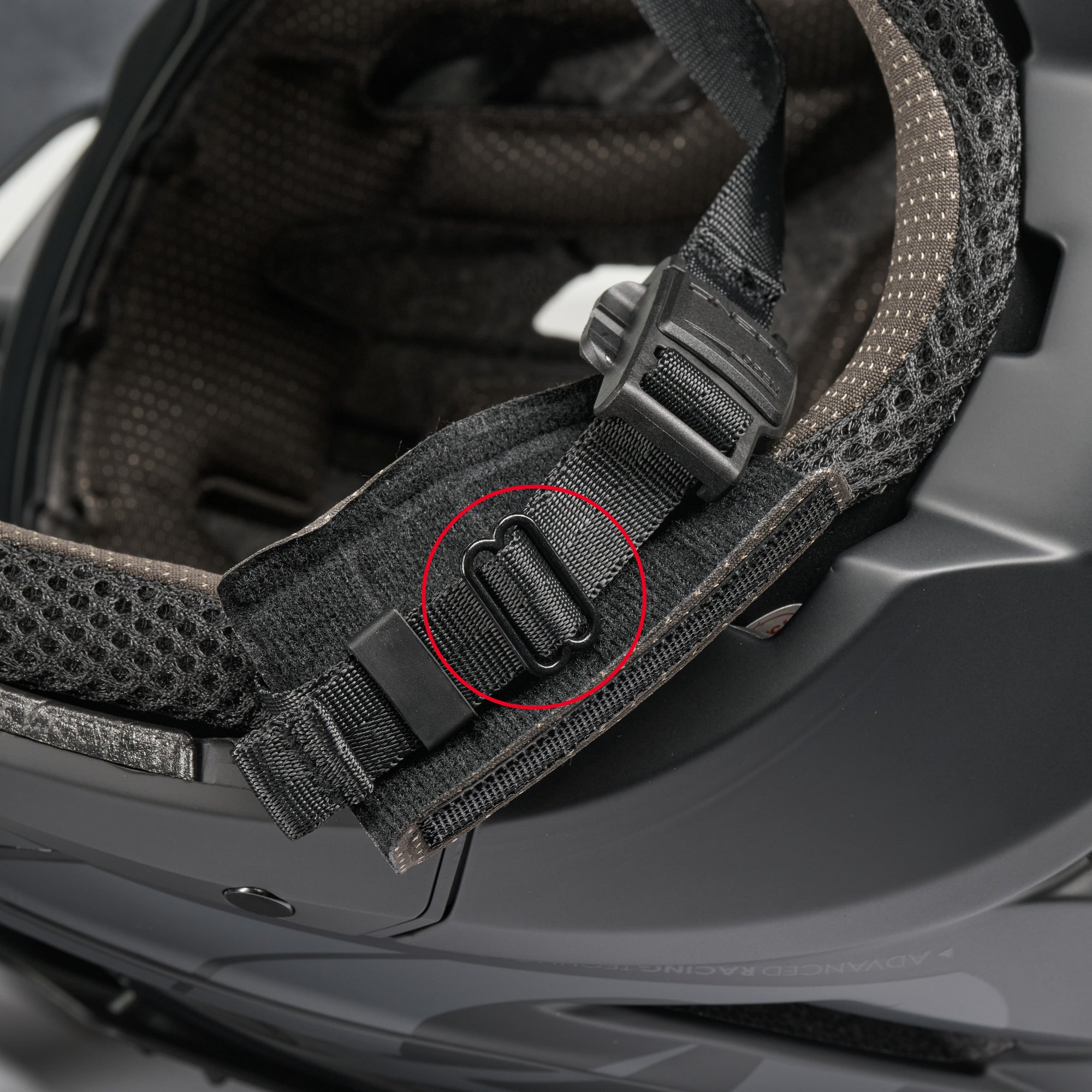 Nahaufnahme des Kinnriemens eines schwarzen Motorradhelms, mit einem roten Kreis, der die schwarze Kunststoffschnalle auf der Innenpolsterung hervorhebt.
