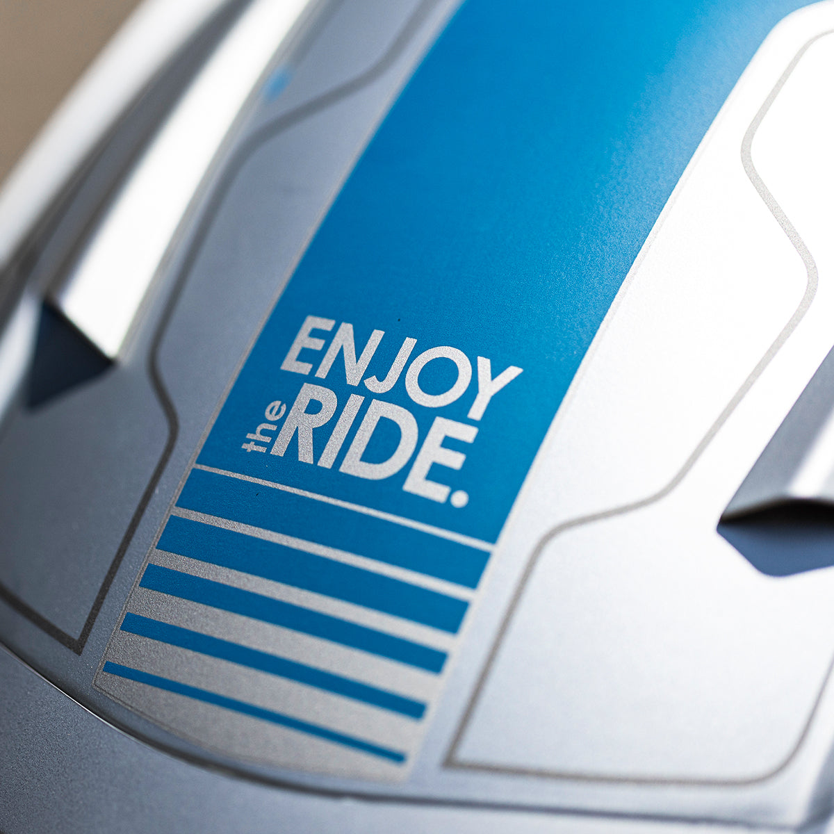 Nahaufnahme eines blauen und silbernen Objekts mit der Aufschrift "ENJOY the RIDE." in weißer Schrift, umgeben von weißen Linien und geometrischen Formen.