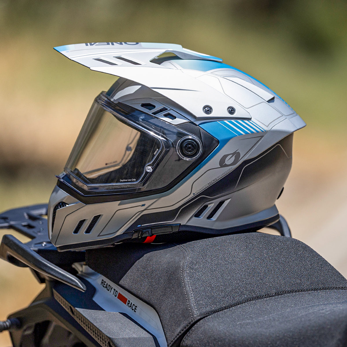 Ein moderner, weiß-blauer Motorradhelm mit Visier und aerodynamischem Design ruht auf einem schwarzen Sitz im Freien.