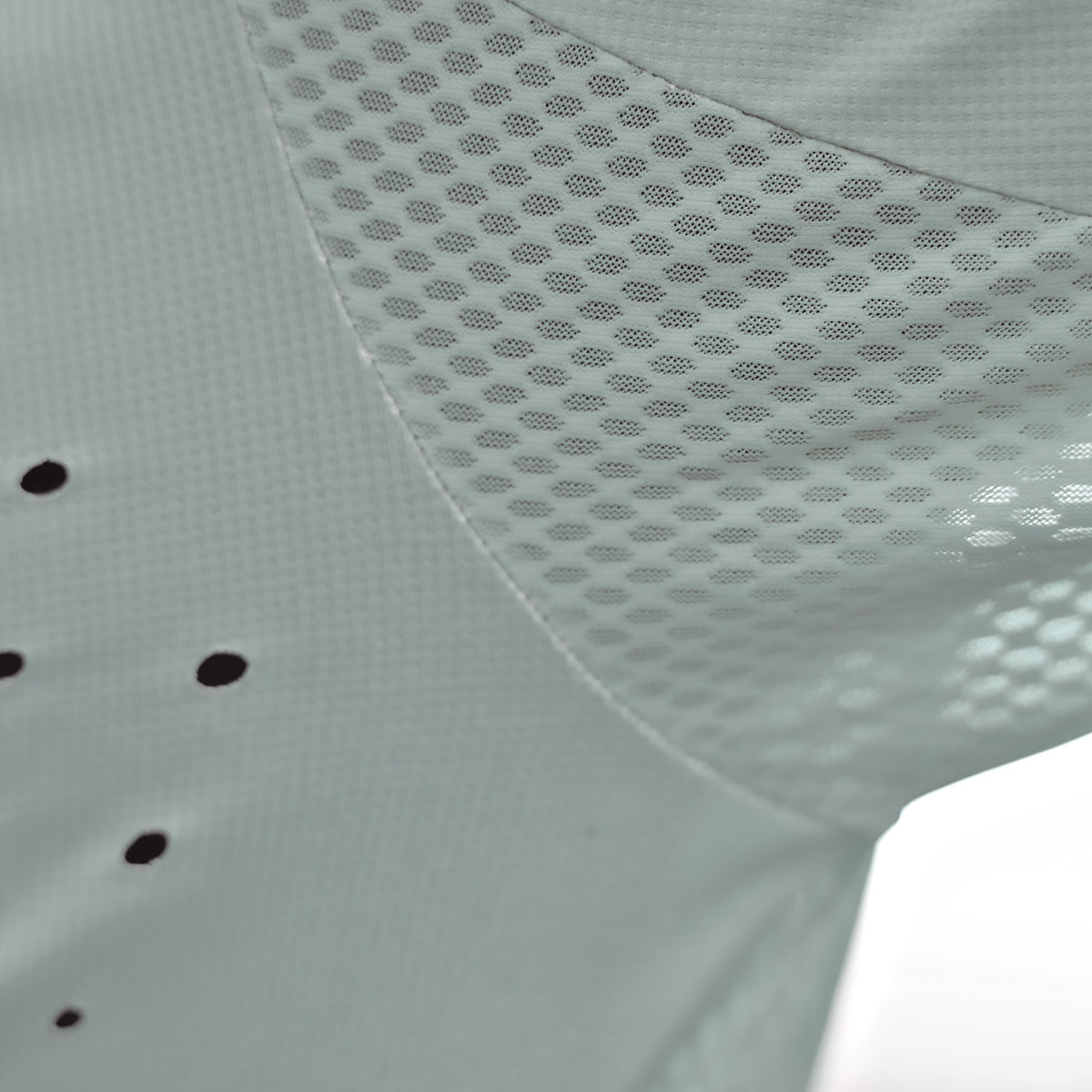 Nahaufnahme eines hellgrauen Stoffes mit Netzstruktur und kleinen Perforationen, der sowohl geschlossene als auch belüftete Bereiche zeigt. Der Stoff wirkt leicht und atmungsaktiv.