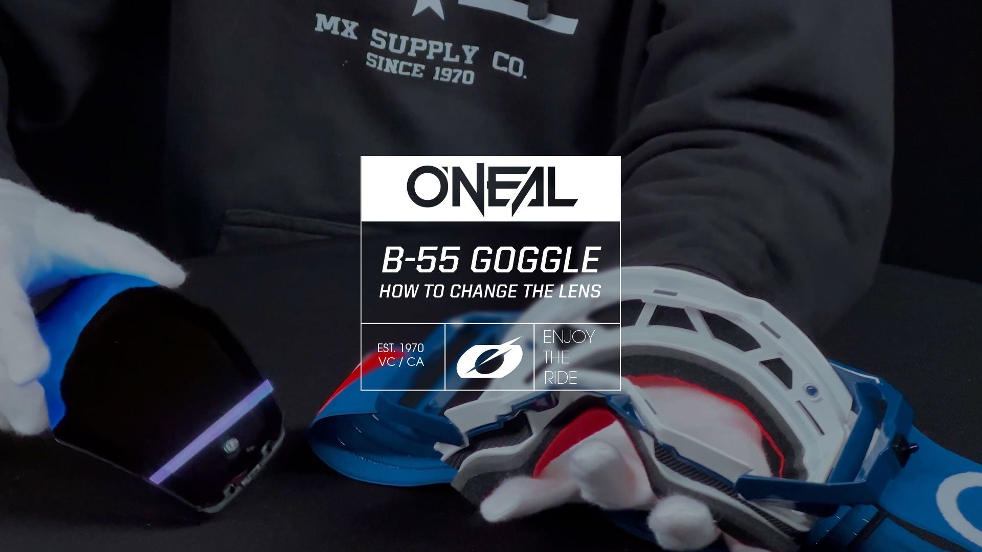 Eine Person in einem schwarzen Hoodie von MX Supply Co. hält eine O'Neal B-55-Brille und bearbeitet sie mit einem Werkzeug. Der Text auf dem Bild lautet: „O'Neal B-55-Brille: So wechseln Sie die Linse.“.
