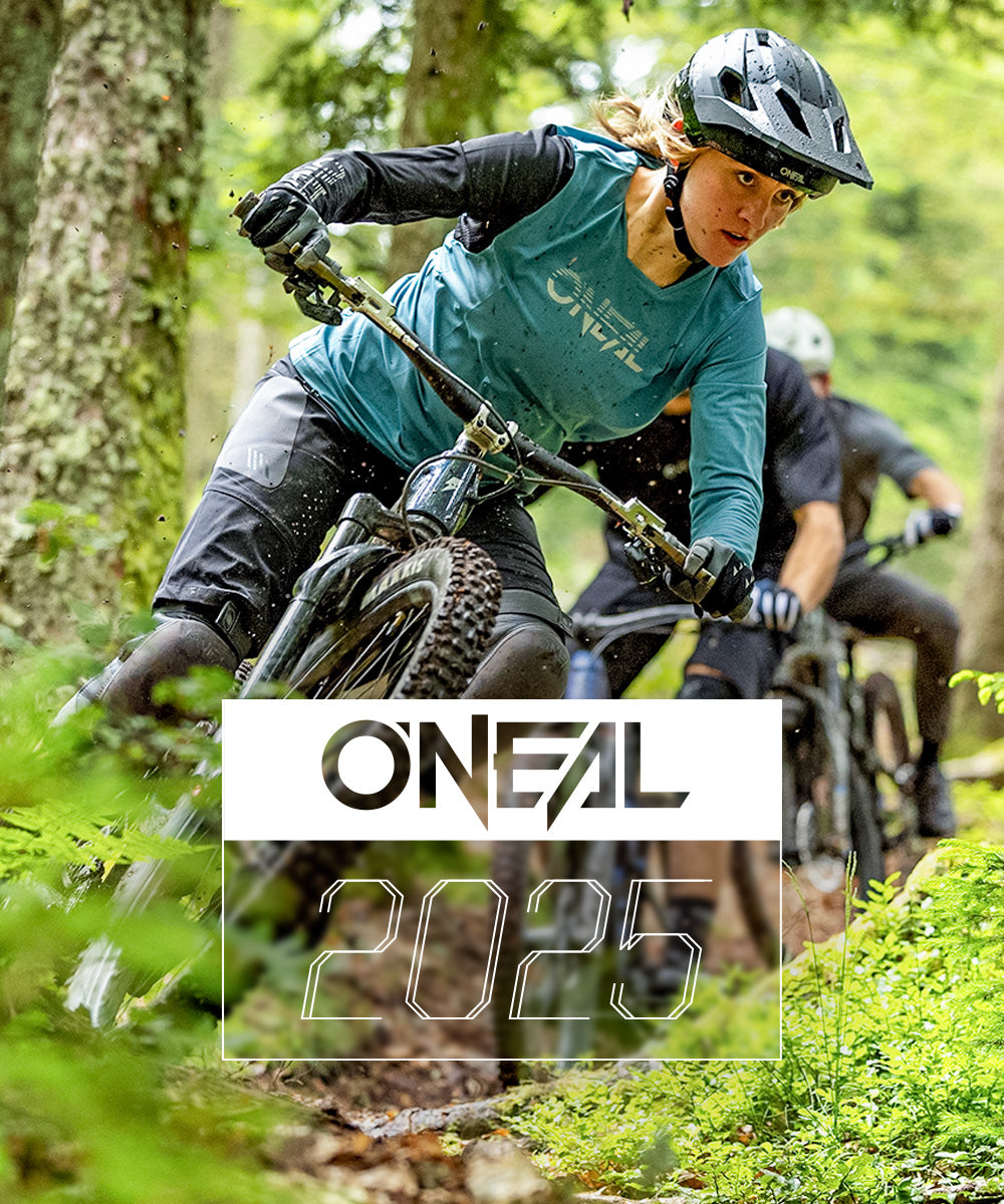 Ein Radfahrer in blaugrüner O'Neal-Ausrüstung fährt mit einem Mountainbike einen Waldweg entlang, gefolgt von einem anderen Radfahrer. Am unteren Bildrand erscheint der Text „O'NEAL 2025“.