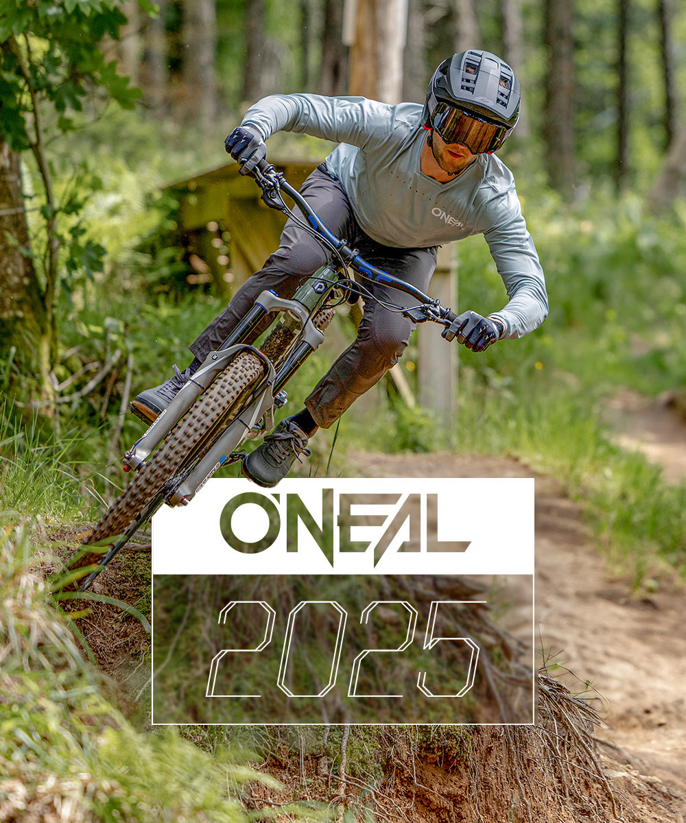 Ein Mountainbiker mit Helm, Schutzbrille und O’NEAL-Ausrüstung fährt einen Waldweg entlang. Das O’NEAL-Logo und die „2025“ sind in fettem weißen Text im Vordergrund deutlich zu sehen.