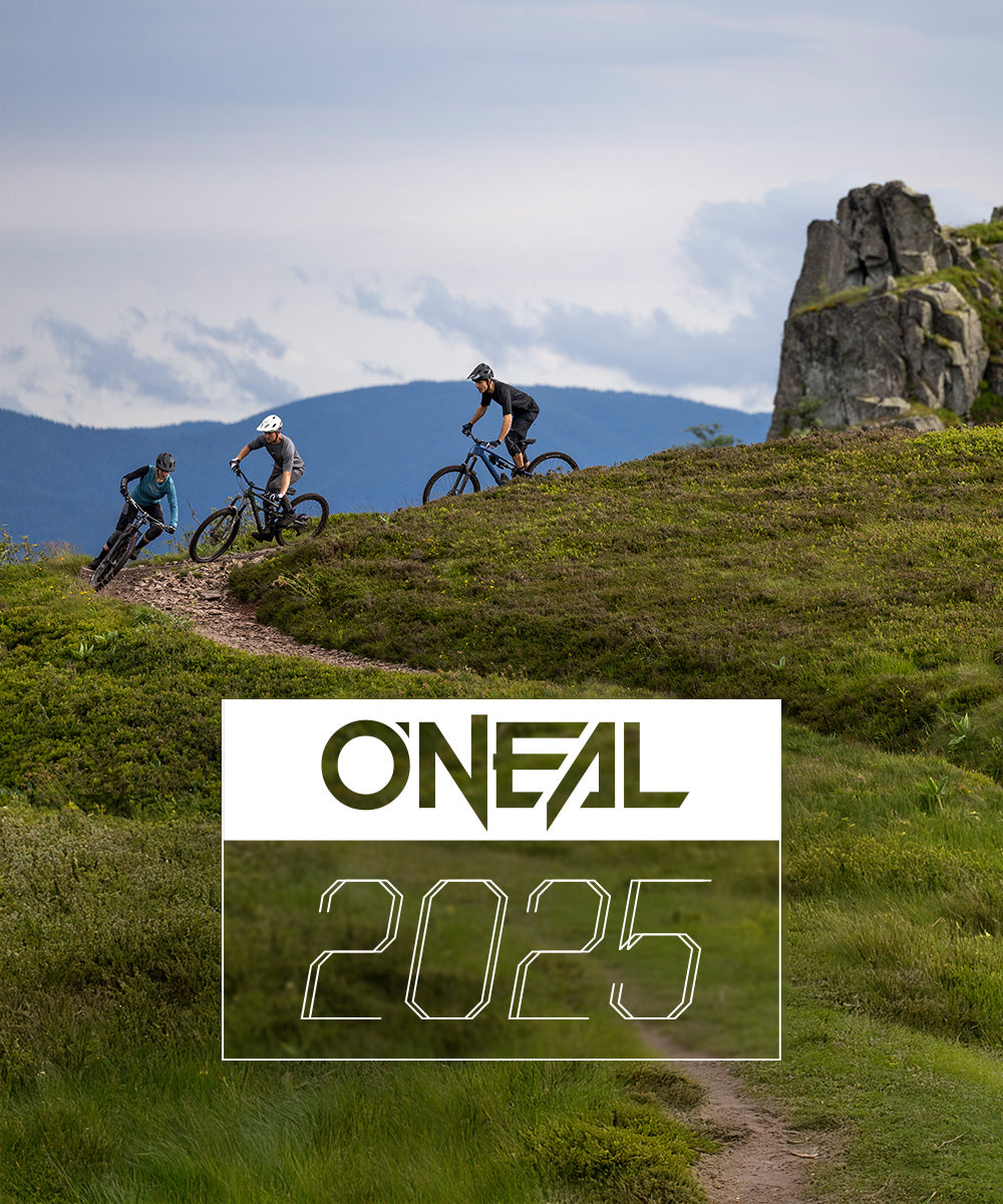 Drei Mountainbiker fahren auf einem gewundenen Feldweg durch grüne Hügel mit Felsvorsprüngen. Der Himmel ist bewölkt. Der Text „O'Neal 2025“ ist am unteren Bildrand eingeblendet.