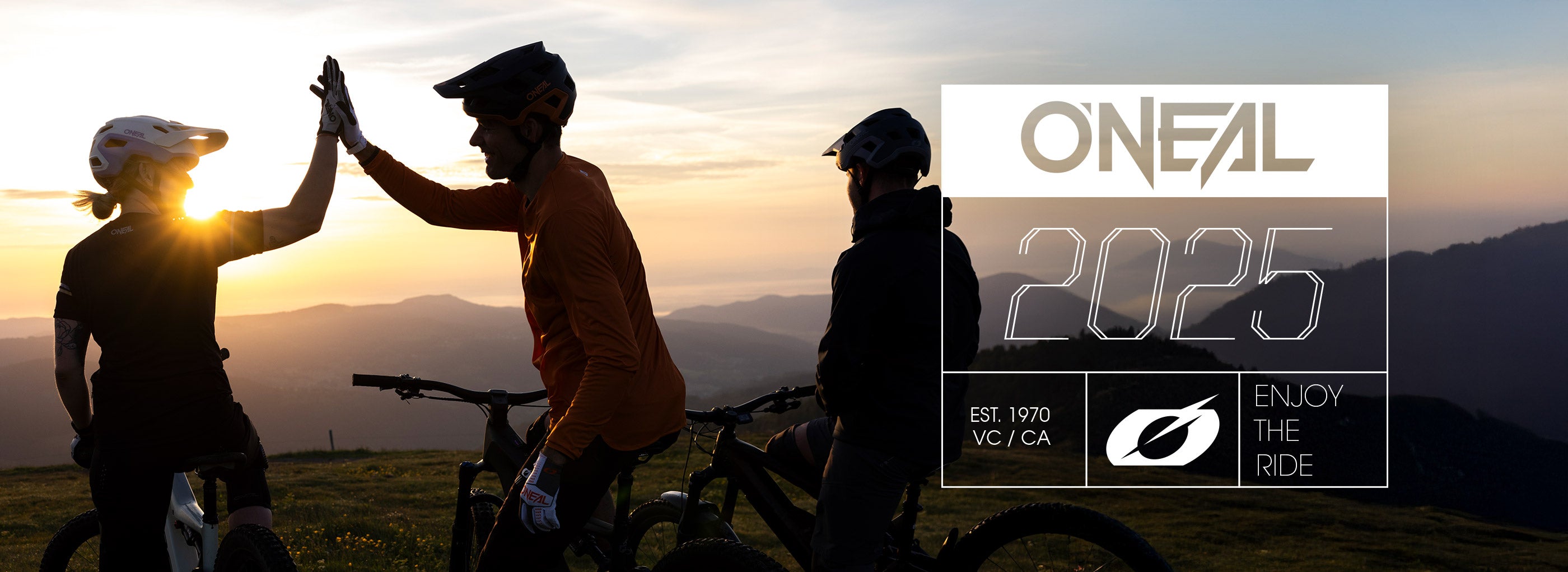Drei Mountainbiker, die sich auf einem Hügel vor dem Sonnenuntergang abheben, geben sich neben ihren Fahrrädern ein High Five. Der Text im Overlay lautet: „ONEAL 2025“, „ENJOY THE RIDE“ und „EST. 1970 VC/CA.“.