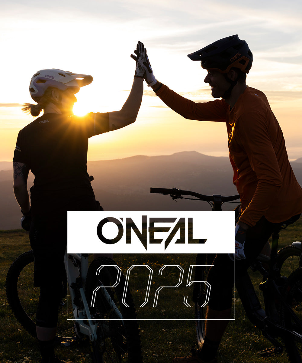 Zwei Mountainbiker mit Helmen geben sich bei Sonnenuntergang ein High-Five, im Hintergrund die Berge. Das O'NEAL-Logo und der Text „2025“ sind unten im Bild eingeblendet.