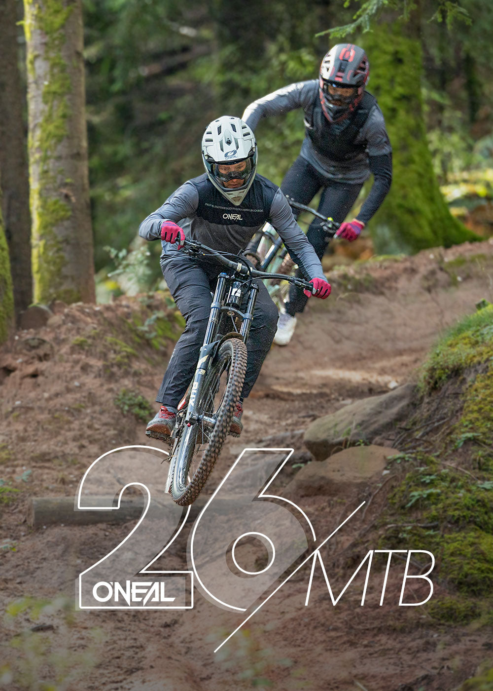 Zwei Mountainbiker mit Helmen und Ausrüstung fahren mit hoher Geschwindigkeit einen Waldweg hinunter, der von Bäumen und Grünflächen umgeben ist. Der fettgedruckte weiße Text auf dem Bild lautet "26/O'NEAL/MTB.