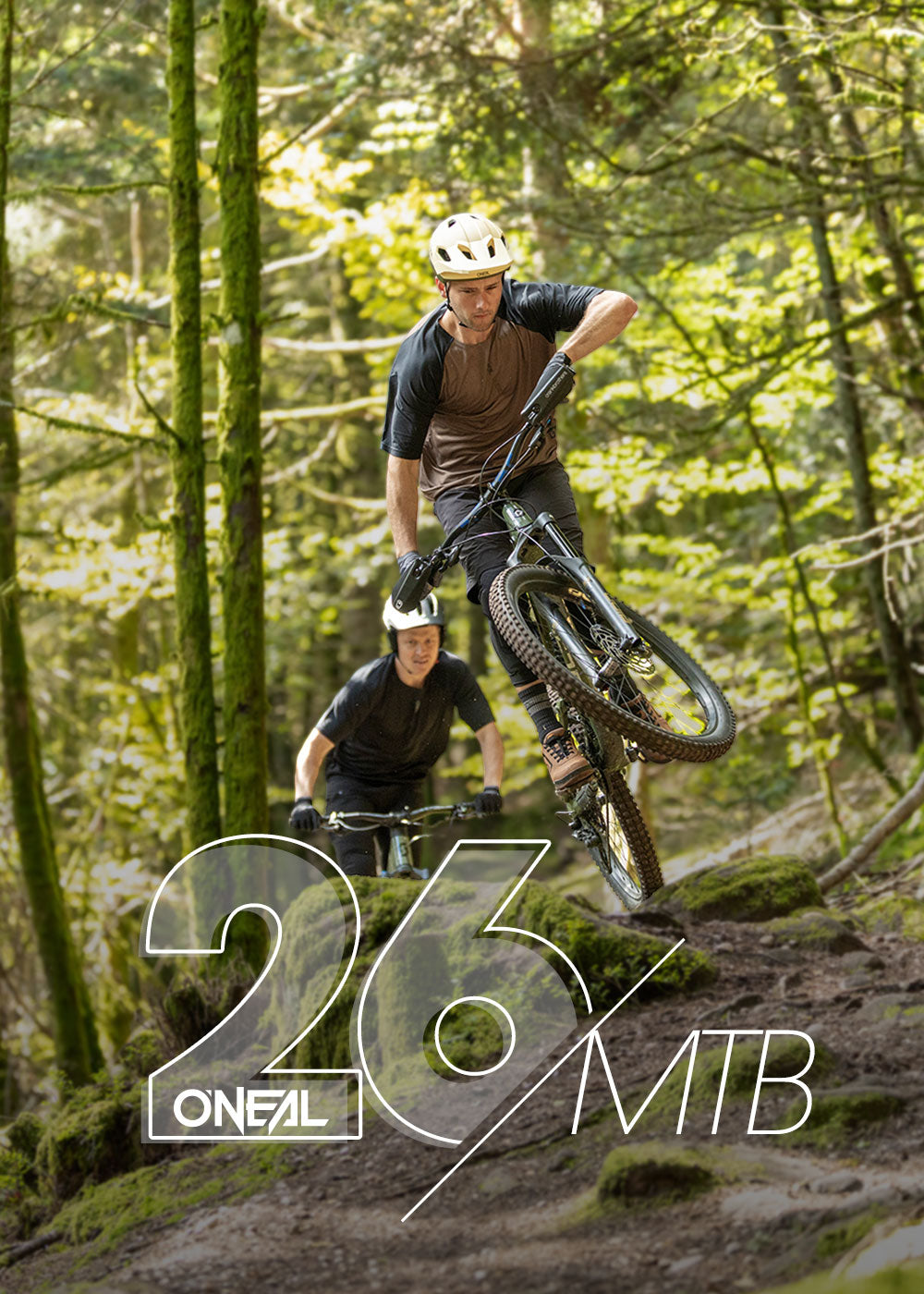 Zwei Mountainbiker fahren durch einen üppigen Wald; der vordere Fahrer hebt das Vorderrad seines Fahrrads vom Boden ab und macht einen Wheelie. Das Sonnenlicht fällt durch die Bäume. Der Text lautet "O'NEAL 26/MTB.".