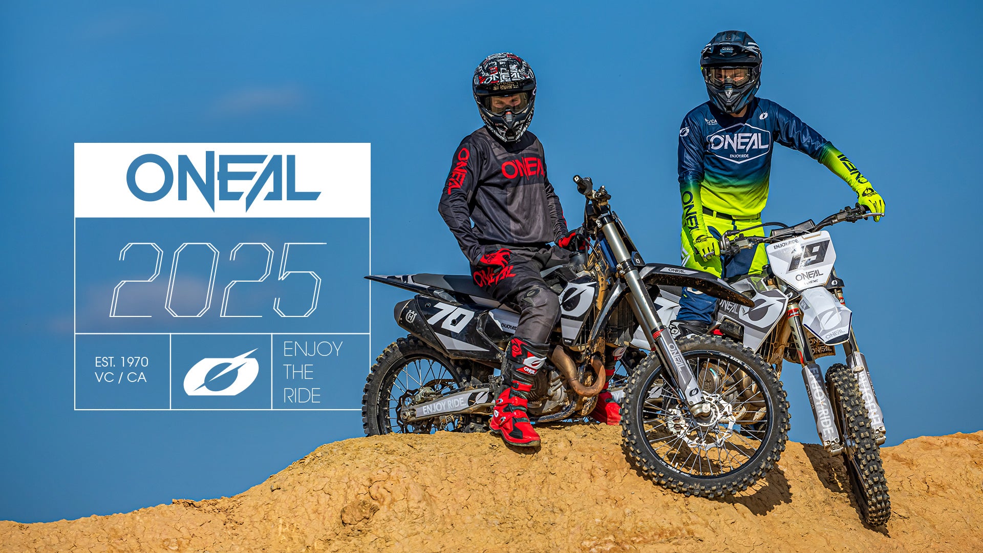 Zwei Motocross-Fahrer in O’Neal-Ausrüstung posieren mit ihren Dirtbikes auf einem sandigen Hügel unter blauem Himmel. Der Text lautet: „ONEAL 2025. Viel Spaß beim Fahren. Gegründet 1970 VC/CA“ mit O’Neals Logo.