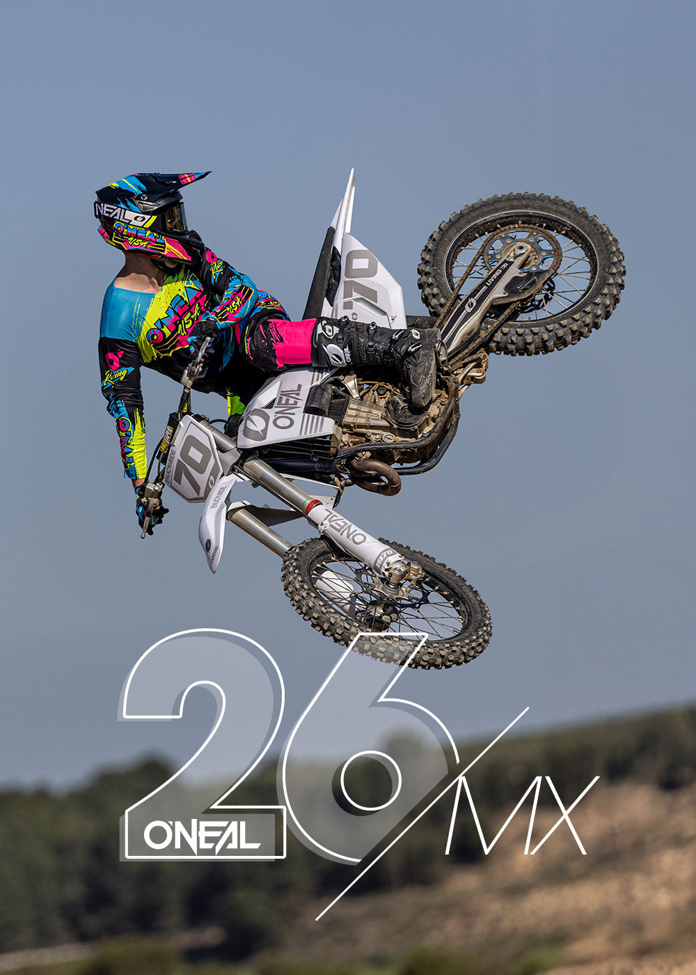 Ein Motocross-Fahrer in farbenfroher Ausrüstung vollführt einen hohen Sprung auf einem Dirt Bike, seitlich in der Luft gegen einen klaren Himmel. Die Nummer 26 und das O'NEAL MX-Logo sind am unteren Rand des Bildes zu sehen.