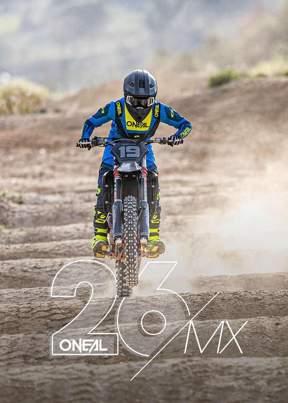 Ein Motocross-Fahrer in blauer und gelber O'NEAL-Kleidung fährt mit einem Dirt Bike auf einer unebenen Strecke und wirbelt dabei Staub auf. Die Nummer 19 ist auf dem Motorrad zu sehen. Das Bild zeigt den Text "23 O'NEAL MX" in großen weißen Buchstaben.