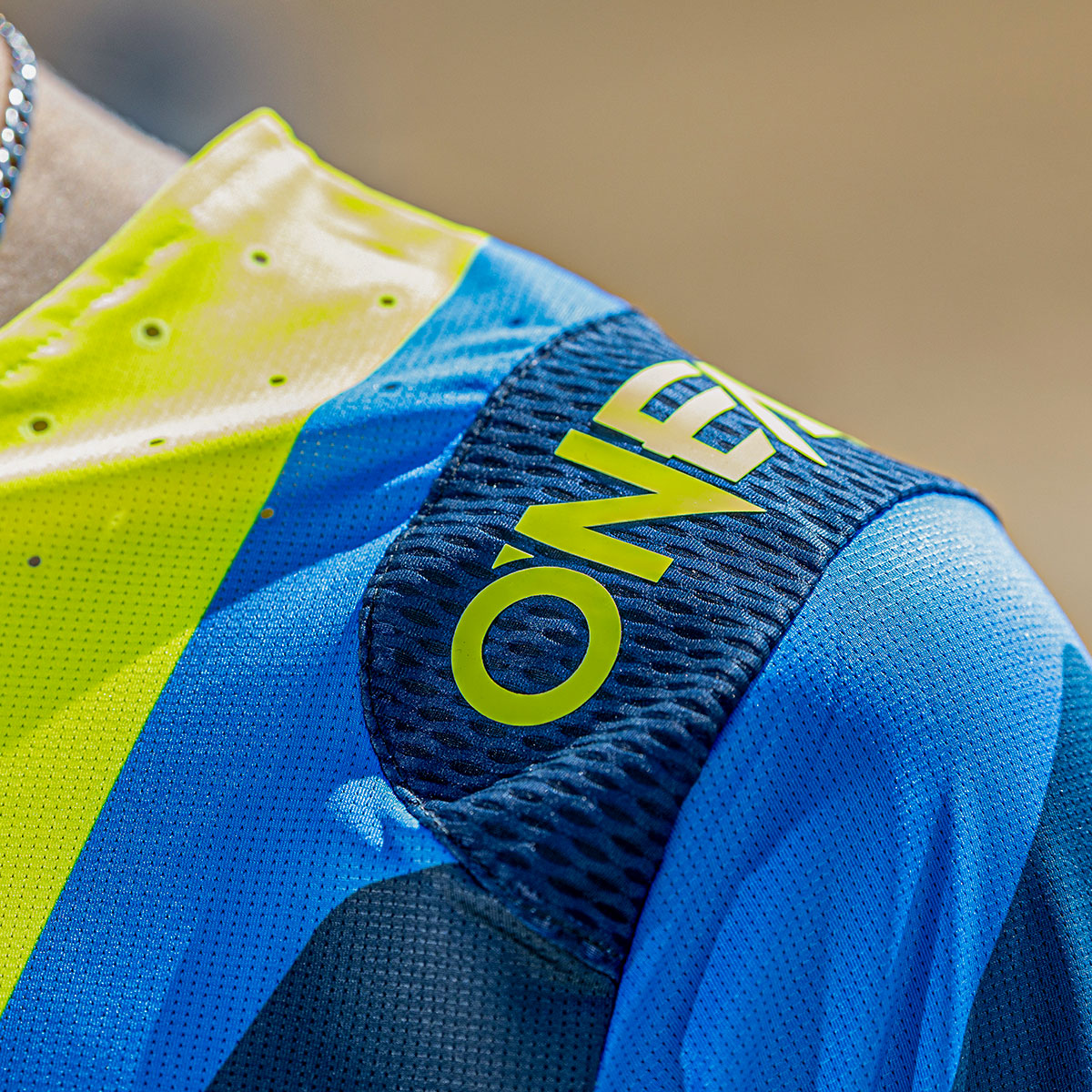 Nahaufnahme eines blau-gelben Sporttrikots mit der Aufschrift "ONEAL" in gelben Buchstaben auf der Schulter. Der Stoff erscheint strukturiert und atmungsaktiv, mit kontrastreichen Farben und sichtbaren Nähten.