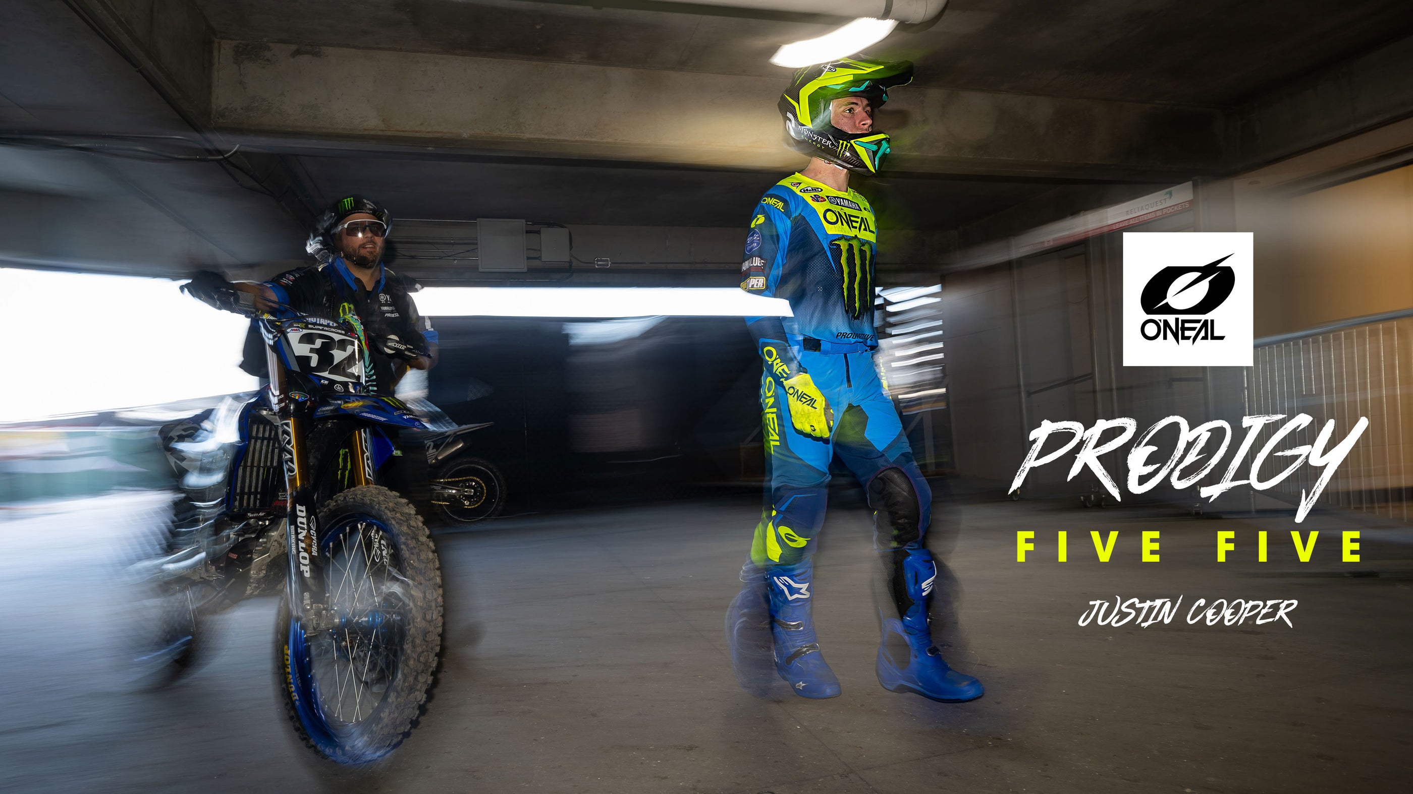Zwei Motocross-Fahrer in blau-gelber O’Neal-Ausrüstung, einer zu Fuß, der andere auf einem Motorrad mit der Nummer 32, stehen unter einer Betonkonstruktion. Der Text lautet „O’NEAL PRODIGY FIVE FIVE JUSTIN COOPER“.