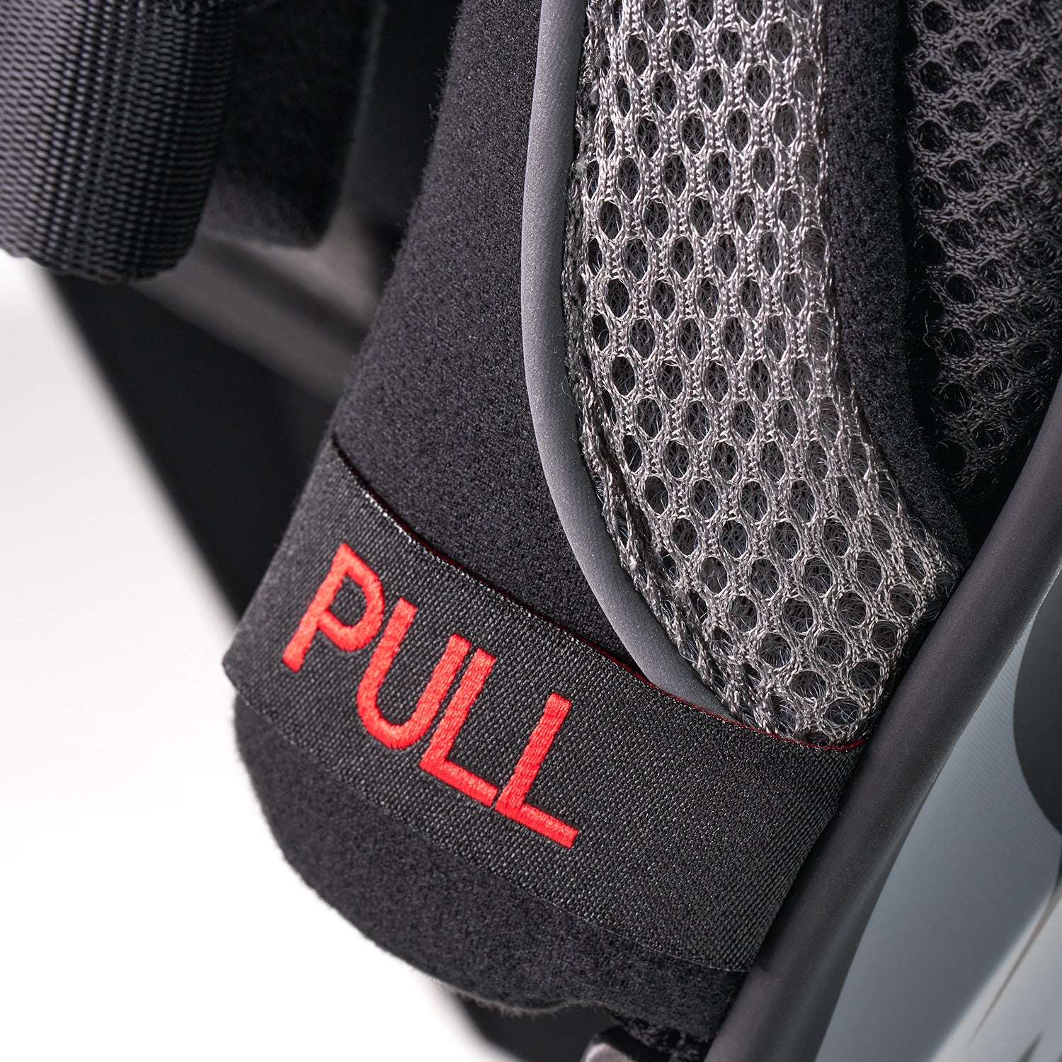 Nahaufnahme eines schwarzen Stoffbandes mit dem in fetten roten Buchstaben aufgestickten Wort „PULL“, befestigt an einem Netz- und Schaumstoffmaterial, möglicherweise Teil einer Sicherheits- oder Sportausrüstung.