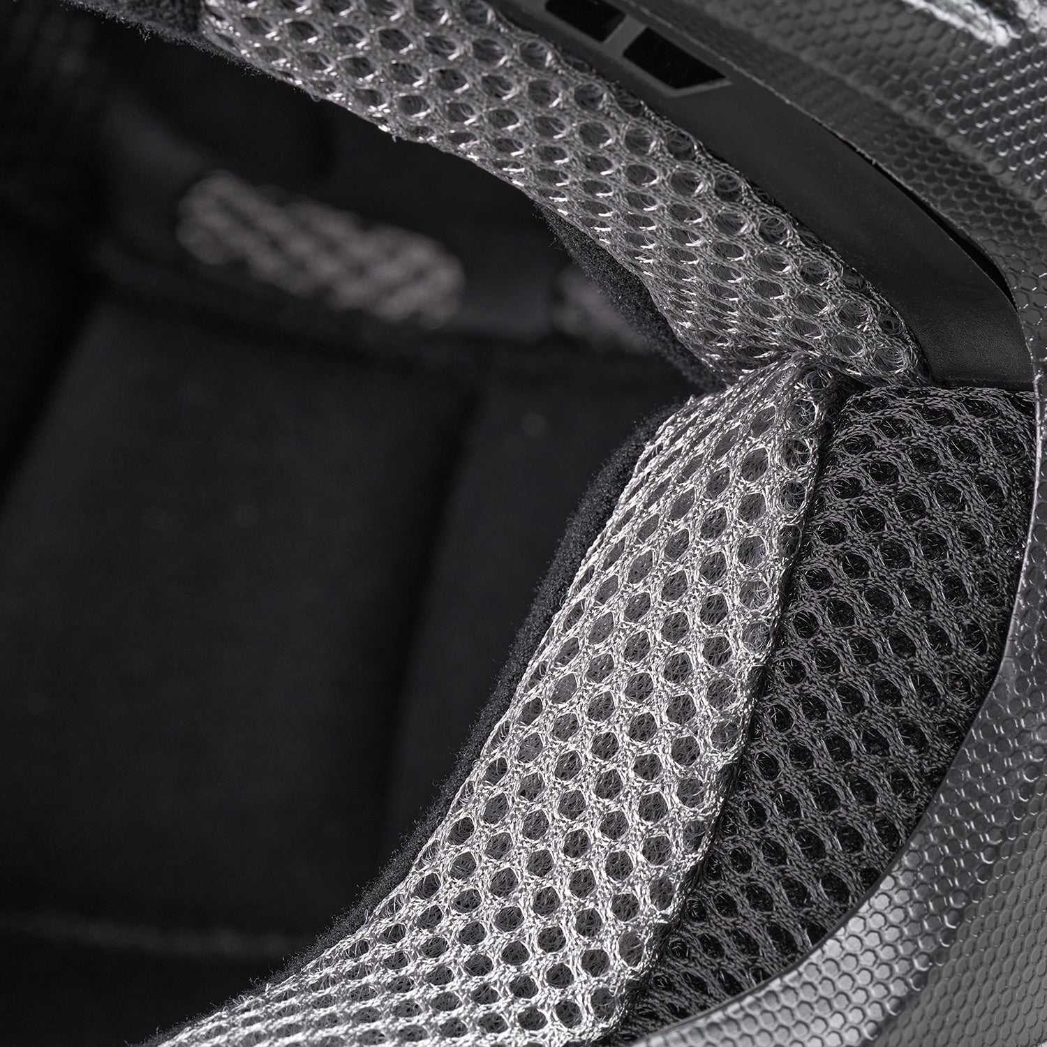 Nahaufnahme der Netzpolsterung und des Futters im Inneren eines Helms mit detaillierter Textur und atmungsaktivem Material in Schwarz- und Grautönen.