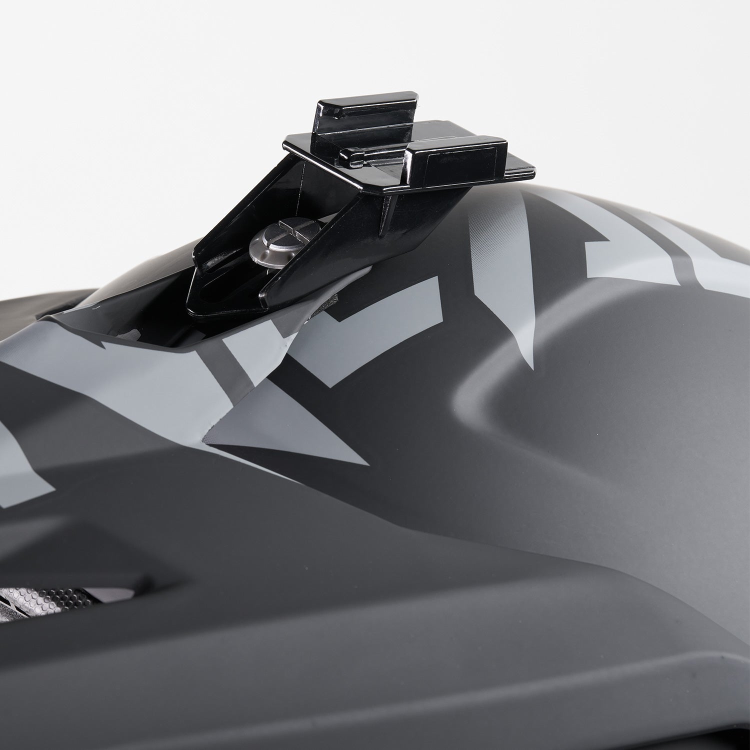 Nahaufnahme eines mattschwarzen Helms mit einem geometrischen grauen Muster und einer schwarzen Montagehalterung an der Oberseite.