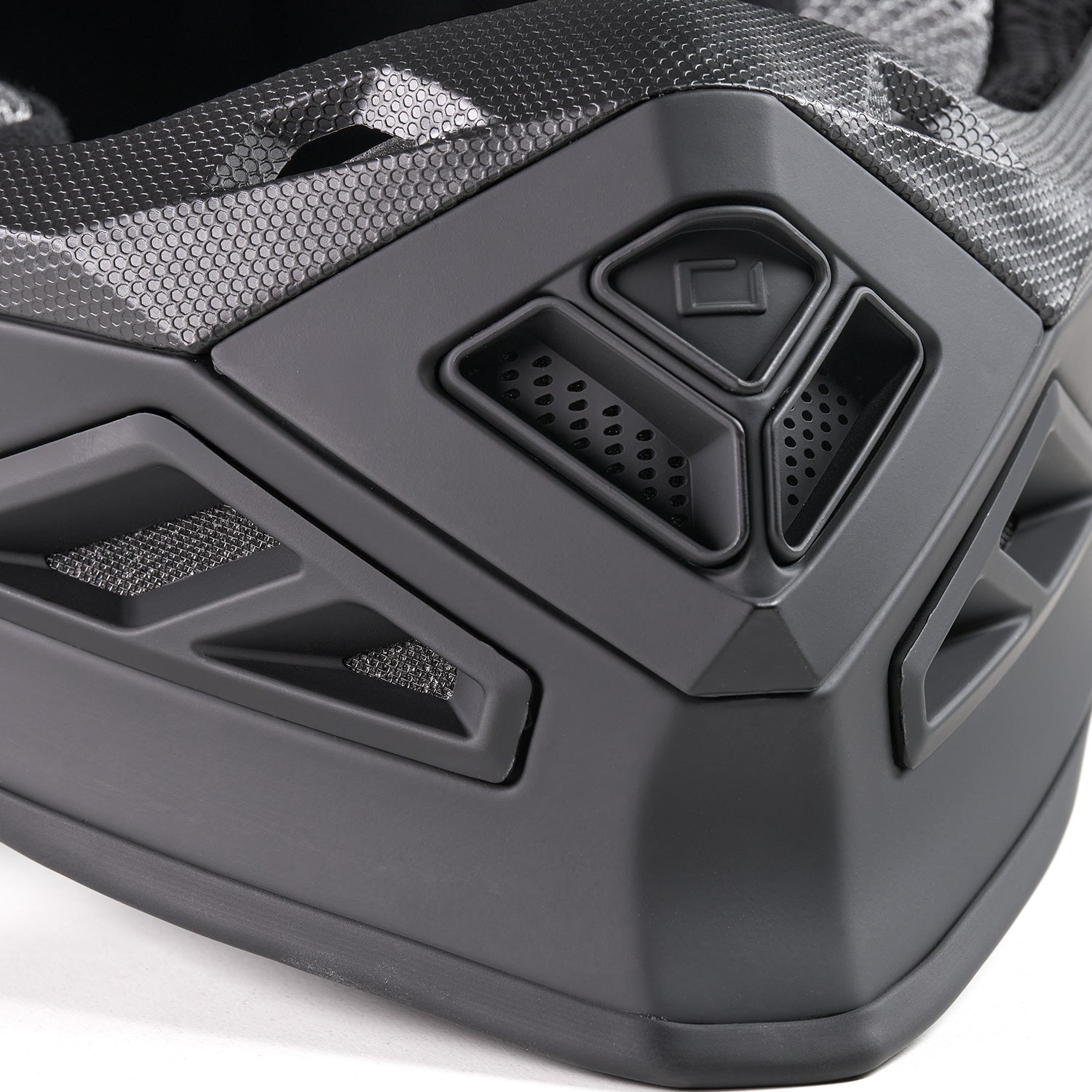 Nahaufnahme des unteren vorderen Abschnitts eines matt- und glänzend-schwarzen Integralhelms mit detaillierten Belüftungsplatten und geometrischen Designelementen.