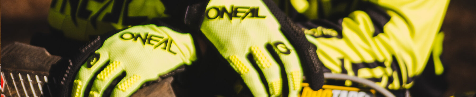 Nahaufnahme einer Person, die leuchtend gelbe Handschuhe mit dem Markennamen „ONEAL“ trägt. Die Handschuhe liegen auf einer Oberfläche, möglicherweise Teil eines Motorrads oder einer Ausrüstung.