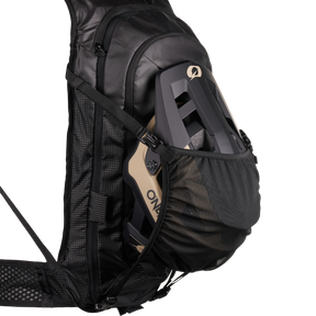 The O'NEAL Europe JUNCTION Protective Backpack in black features a mesh pocket that houses a beige and black bike helmet against a plain white background.