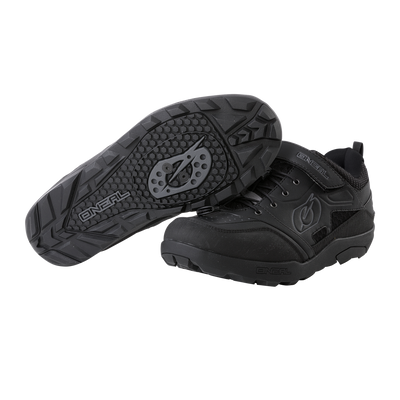 Ein Paar O'NEAL TRAVERSE SPD-Schuhe in Schwarz, ideal für Motorsport-Zubehör, vor weißem Hintergrund. Ein Schuh ist so positioniert, dass das untere Profil mit einem markanten kreisförmigen Griffmuster für perfekten Halt hervorgehoben wird, während der andere Schuh das Seitenprofil und die Schnürsenkel hervorhebt und mit dem O'NEAL-Markenlogo und einem Klettverschluss versehen ist.