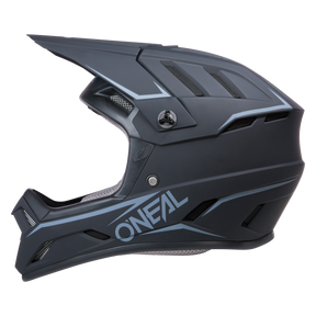 Der O'NEAL BACKFLIP Helm SOLID ist ein mattschwarzer Integralhelm für Motorradfahrer mit kantigen Designelementen und markantem Kinnschutz, passend für Mountainbike-Experten. Dieser Helm verfügt über Belüftungsschlitze und trägt den Markennamen „O'NEAL“ in großen weißen Lettern prominent an der Seite. Seine auf Sicherheit ausgelegte Innenpolsterung ist durch die Öffnungen sichtbar.
