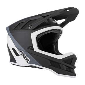 Der O'NEAL BLADE Hyperlite Helm CHARGER ist ein schwarz-weißer Integralhelm mit eckigen Designelementen und einem Visier. Dieser Fiberglas-MTB-Helm verfügt über Belüftungslöcher und aufwendige Details an den Seiten, wobei das O'NEAL-Logo prominent in Weiß an der Seite angebracht ist.
