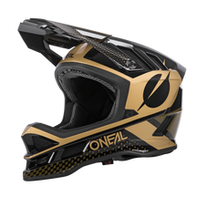 Seitenansicht des O'NEAL BLADE Polyacrylite Helm ACE, einem schwarz-goldenen Integralhelm von O'NEAL. Dieser Helm zeichnet sich durch ein markantes Visier, ein aerodynamisches Design und ein auffälliges geometrisches Muster aus. Der Markenname ist auf der Unterseite und der Rückseite zu sehen und verfügt über Belüftungsöffnungen.