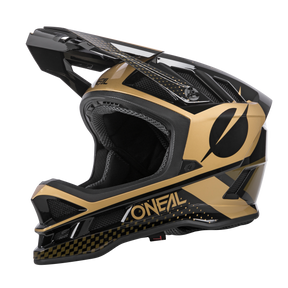 Seitenansicht des O'NEAL BLADE Polyacrylite Helm ACE, einem schwarz-goldenen Integralhelm von O'NEAL. Dieser Helm zeichnet sich durch ein markantes Visier, ein aerodynamisches Design und ein auffälliges geometrisches Muster aus. Der Markenname ist auf der Unterseite und der Rückseite zu sehen und verfügt über Belüftungsöffnungen.