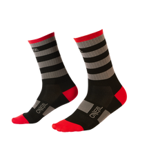 Die O'NEAL MTB Performance Socke STRIPE sind schwarze Radsocken mit roten Fersen und Zehen, verziert mit grauen und schwarzen horizontalen Streifen auf schlichtem schwarzem Hintergrund. „O'NEAL“ ist in Weiß auf den Zehen und an den Seiten deutlich zu sehen, was diese Socken perfekt für Actionsport-Enthusiasten macht, die Schutz suchen.