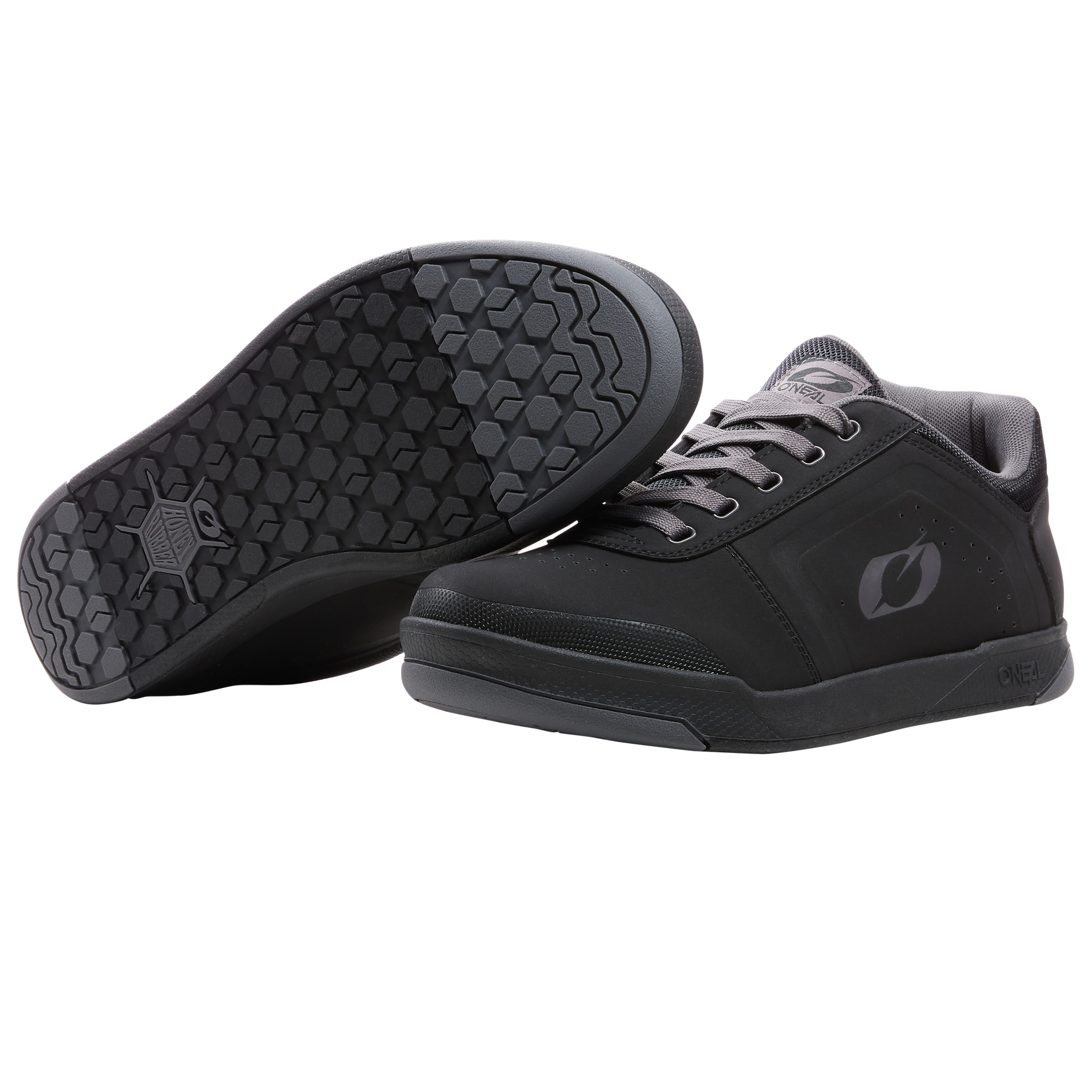 Ein Paar O'NEAL PINNED PRO FLAT Pedal Schuhe in schwarz mit grauen Schnürsenkeln. Ein Schuh zeigt das O'NEAL-Logo aufrecht, während der andere die sechseckige, strukturierte Sohle zeigt - perfekt für Radsportbegeisterte.