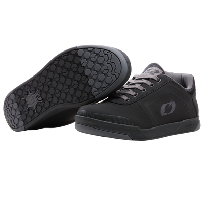 Ein Paar O'NEAL PINNED PRO FLAT Pedal Schuhe in schwarz mit grauen Schnürsenkeln. Ein Schuh zeigt das O'NEAL-Logo aufrecht, während der andere die sechseckige, strukturierte Sohle zeigt - perfekt für Radsportbegeisterte.