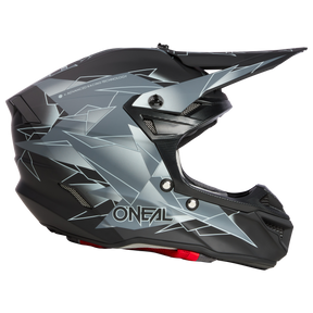 Ein schwarzer Motorradhelm mit einem schlanken Design mit eckigen, silbernen geometrischen Mustern. Der Helm verfügt über Belüftungsöffnungen und einen Kinnschutz. Der Markenname „O’NEAL 5SRS Polyacrylite Helm SURGE“ ist deutlich auf der Seite aufgedruckt und zeigt seine hochwertige Verarbeitung.
