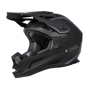 Der O'NEAL DROP DH Helm SOLID ist ein mattschwarzer Integralhelm mit blaugrauen Akzenten. Er verfügt über ein eckiges Visier und einen Kinnschutz, auf dessen Seite der Markenname „O'Neal“ in Weiß zu sehen ist. Dieser aerodynamische Helm ist für das Offroad-Biken konzipiert und bietet sowohl Sicherheit als auch Komfort.