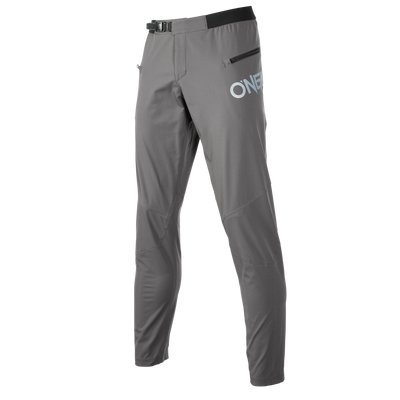 Die O'NEAL TRAILFINDER Hose ist eine schmal geschnittene, graue Sporthose mit elegantem Design. Sie verfügt über einen kleinen Gürtel und eine Schnalle an der Taille, eine Reißverschlusstasche auf der rechten Seite und das Wort „ONE“ ist deutlich auf den oberen Oberschenkelbereich gedruckt. Diese Hose scheint aus leichtem Material gefertigt zu sein.