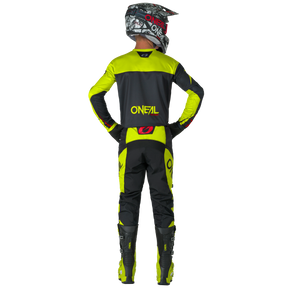 Eine Person in schwarzer und leuchtend gelber Motocross-Ausrüstung mit O'NEAL ELEMENT Pants RACEWEAR und anderer O'NEAL-Bekleidung steht mit den Händen auf den Hüften von der Kamera abgewandt, wobei die Marke "O'NEAL" sichtbar ist.